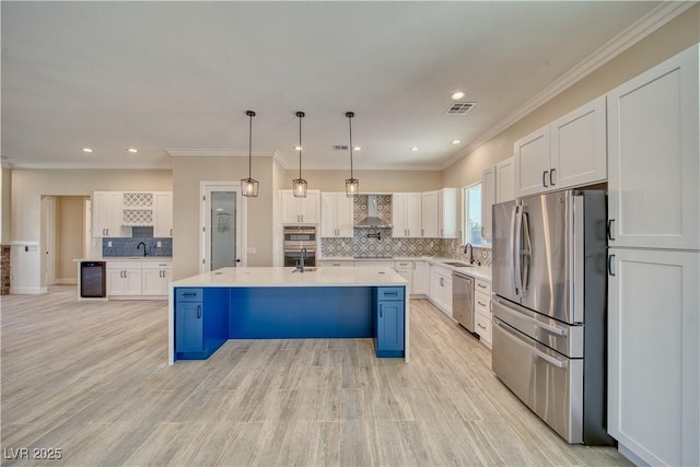 kitchen featuring appliances with stainless steel finishes, white cabinetry, hanging light fixtures, a center island with sink, and wall chimney exhaust hood