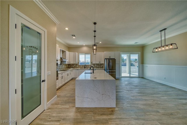 kitchen with stainless steel fridge, decorative light fixtures, an island with sink, and white cabinets