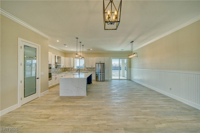 kitchen with white cabinetry, hanging light fixtures, a center island, stainless steel appliances, and wall chimney exhaust hood