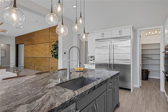 kitchen with gray cabinetry, sink, white cabinets, built in refrigerator, and hanging light fixtures