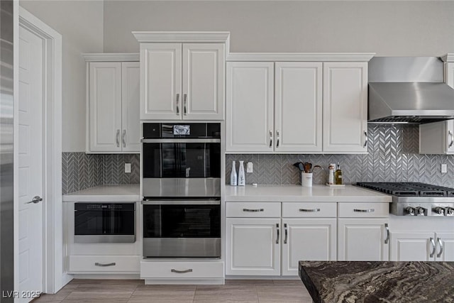 kitchen featuring white cabinets, wall chimney range hood, appliances with stainless steel finishes, and tasteful backsplash