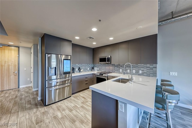 kitchen with kitchen peninsula, appliances with stainless steel finishes, a kitchen bar, sink, and light hardwood / wood-style floors