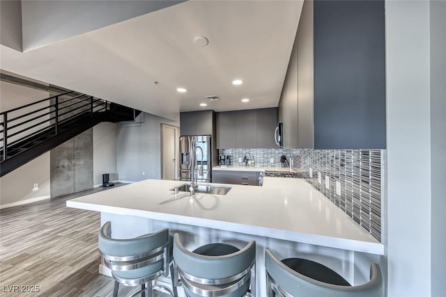 kitchen with gray cabinetry, sink, light hardwood / wood-style floors, kitchen peninsula, and a breakfast bar area