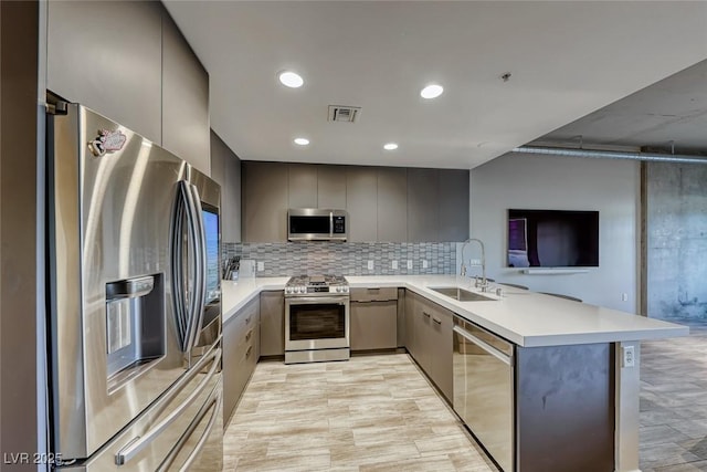 kitchen featuring sink, gray cabinets, appliances with stainless steel finishes, tasteful backsplash, and kitchen peninsula