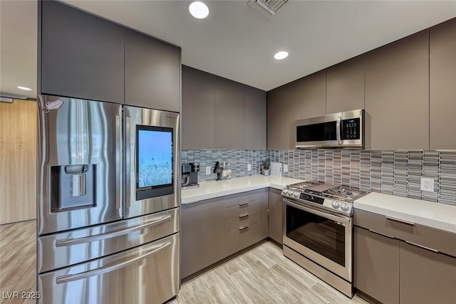 kitchen with backsplash, gray cabinets, light hardwood / wood-style flooring, and appliances with stainless steel finishes