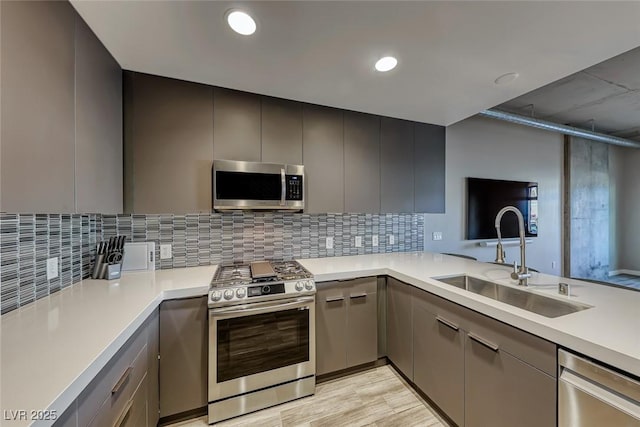 kitchen featuring sink, kitchen peninsula, gray cabinets, decorative backsplash, and appliances with stainless steel finishes