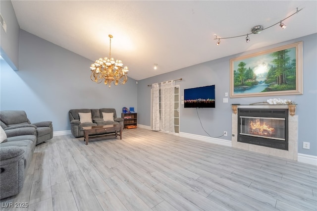 living room featuring a tile fireplace, an inviting chandelier, lofted ceiling, and light wood-type flooring