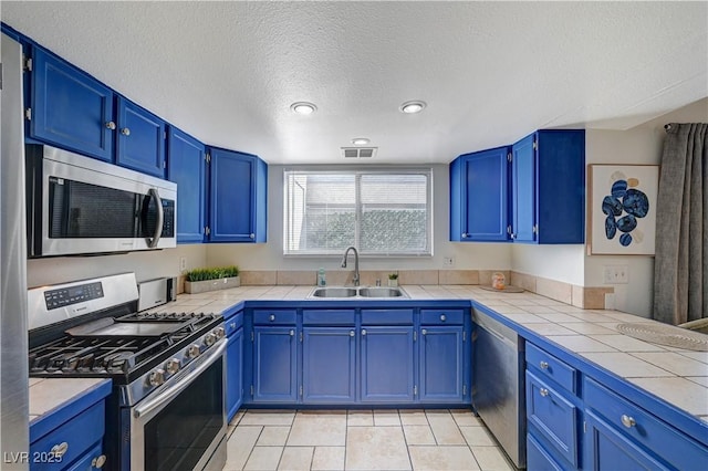 kitchen with blue cabinetry, sink, a textured ceiling, light tile patterned floors, and appliances with stainless steel finishes