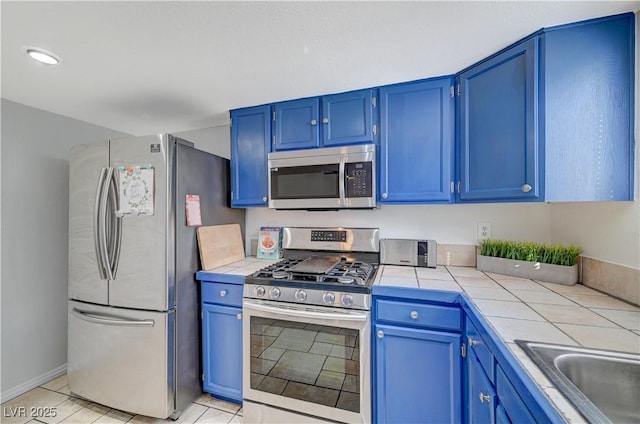 kitchen with blue cabinets, sink, light tile patterned floors, tile counters, and stainless steel appliances