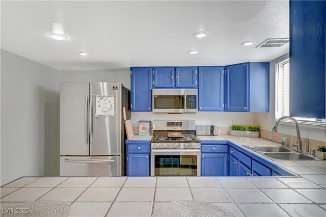 kitchen featuring tile countertops, blue cabinetry, sink, and appliances with stainless steel finishes