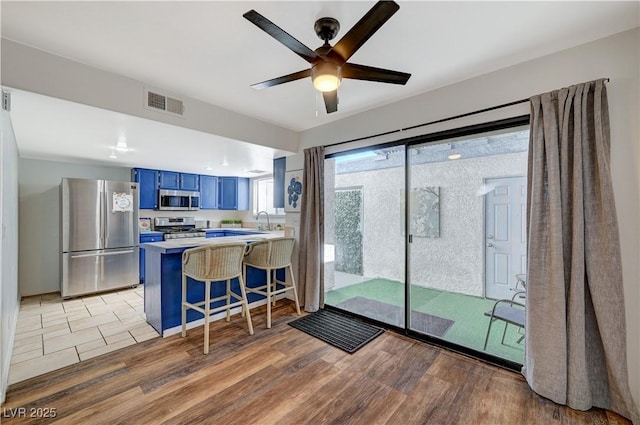 kitchen with kitchen peninsula, appliances with stainless steel finishes, a kitchen breakfast bar, blue cabinets, and sink