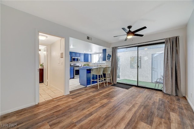 kitchen with kitchen peninsula, appliances with stainless steel finishes, light wood-type flooring, a breakfast bar, and blue cabinets