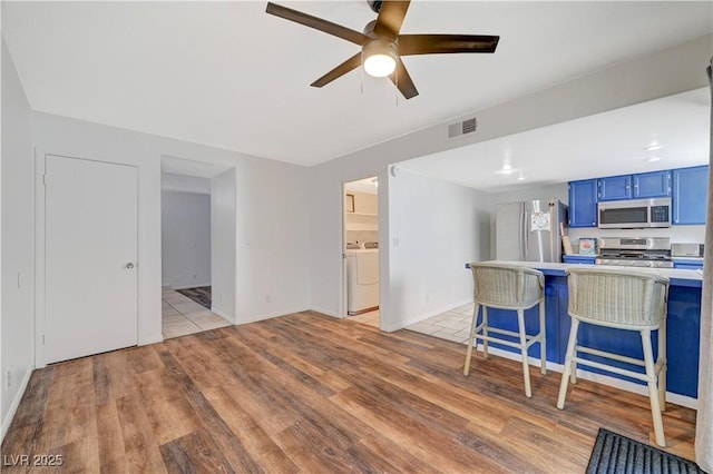 kitchen featuring stainless steel appliances, light hardwood / wood-style flooring, blue cabinets, kitchen peninsula, and a breakfast bar