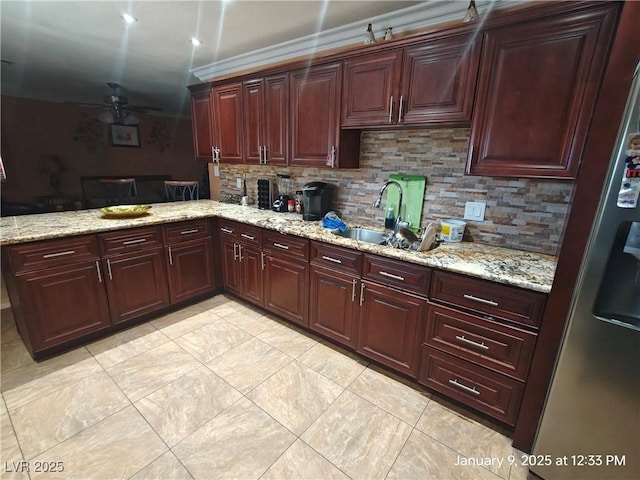 kitchen with backsplash, sink, ceiling fan, light stone countertops, and stainless steel fridge with ice dispenser