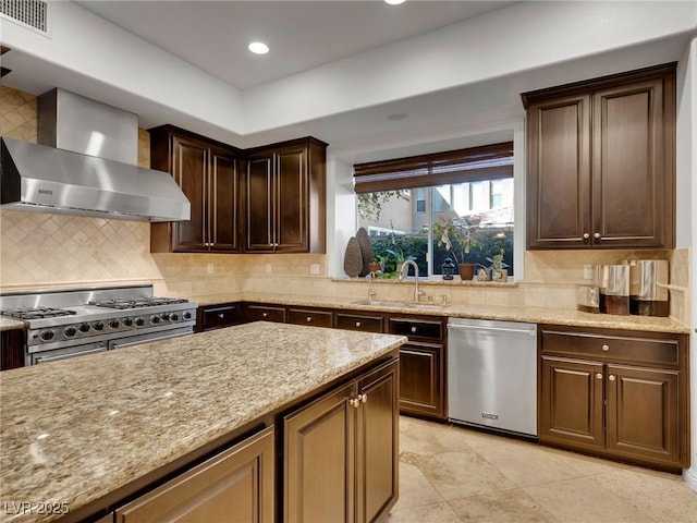 kitchen with sink, light stone counters, dark brown cabinetry, wall chimney range hood, and appliances with stainless steel finishes