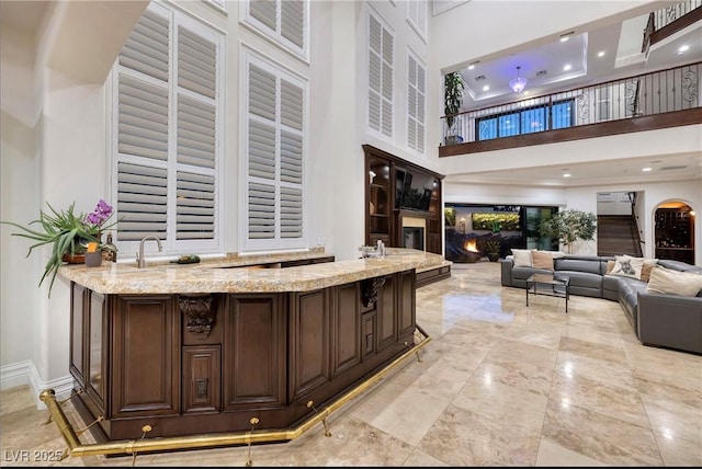 bar with light stone counters, dark brown cabinets, and a high ceiling