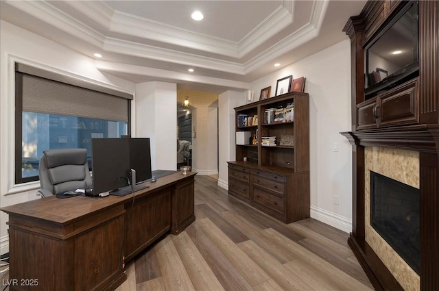 home office featuring a tray ceiling, a tile fireplace, crown molding, and light hardwood / wood-style flooring