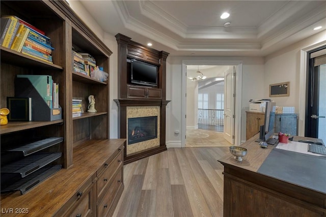 office featuring a tile fireplace, crown molding, a chandelier, light hardwood / wood-style floors, and a tray ceiling