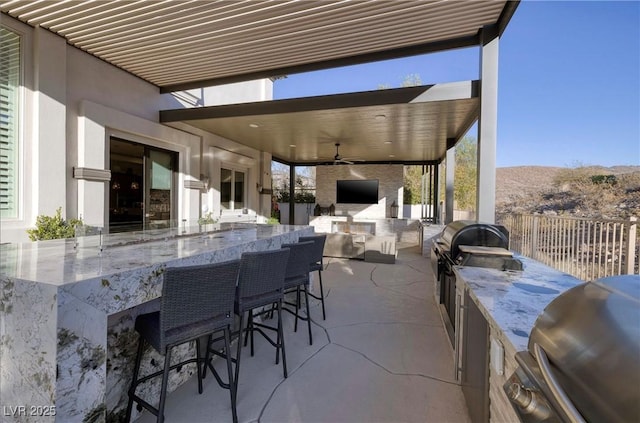 view of patio with area for grilling, ceiling fan, an outdoor bar, and an outdoor kitchen