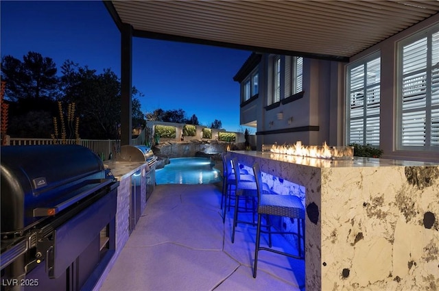 patio at night featuring exterior bar, a grill, and exterior kitchen