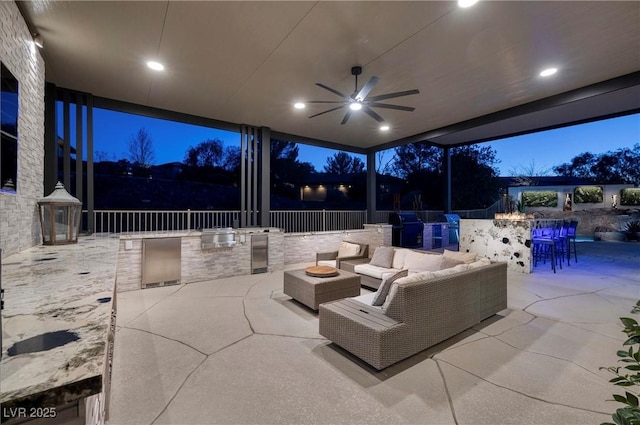 patio terrace at dusk featuring area for grilling, ceiling fan, and exterior kitchen