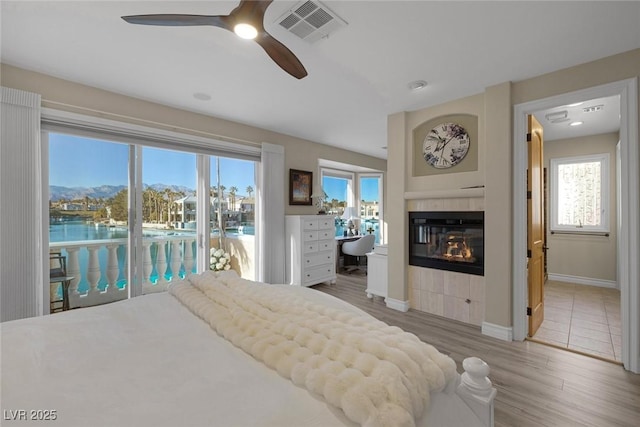 bedroom featuring visible vents, a tile fireplace, wood finished floors, a water view, and access to exterior