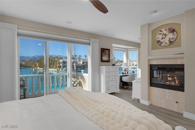 bedroom with multiple windows, wood-type flooring, a fireplace, access to outside, and ceiling fan