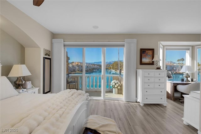 bedroom with access to outside, multiple windows, light wood-type flooring, and a water view