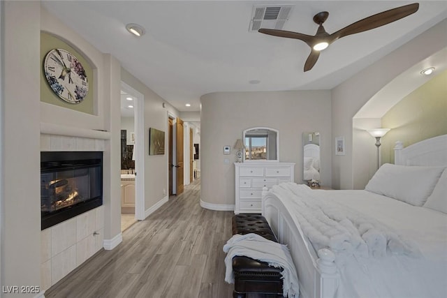 bedroom with visible vents, light wood-style flooring, ceiling fan, a tile fireplace, and baseboards