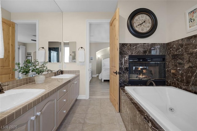 ensuite bathroom with double vanity, ensuite bath, a fireplace, and a sink