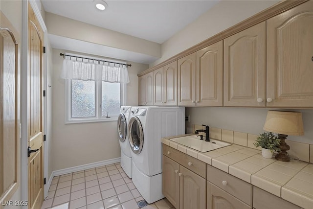 clothes washing area featuring light tile patterned floors, a sink, baseboards, independent washer and dryer, and cabinet space