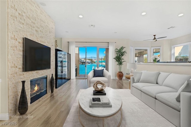 living room with light wood finished floors, a stone fireplace, visible vents, and a healthy amount of sunlight