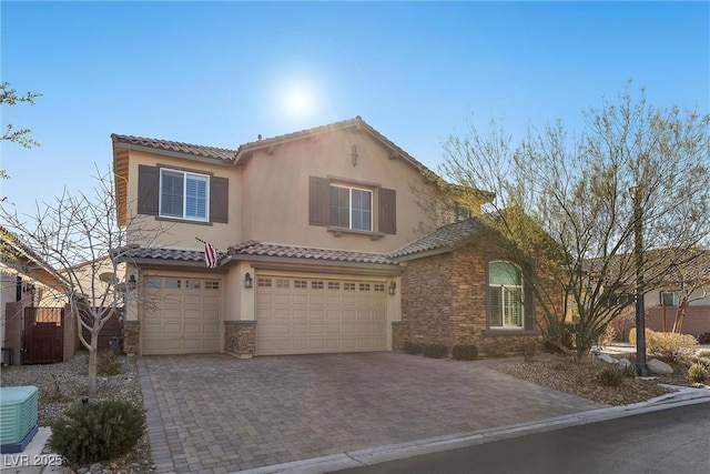 mediterranean / spanish-style house featuring a garage, central AC unit, stone siding, decorative driveway, and stucco siding