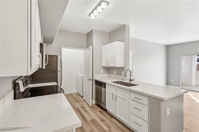 kitchen featuring light wood-style flooring, appliances with stainless steel finishes, white cabinets, a sink, and a peninsula