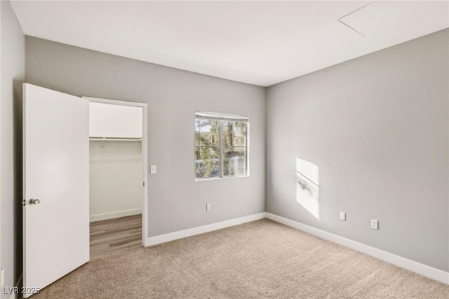 unfurnished bedroom with a walk in closet, a closet, light colored carpet, and baseboards