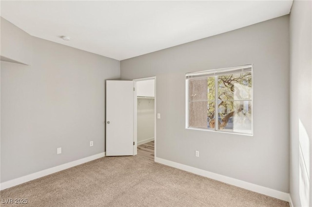 unfurnished bedroom with light carpet, a closet, a walk in closet, and baseboards