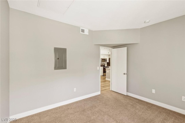 empty room with baseboards, light colored carpet, visible vents, and electric panel