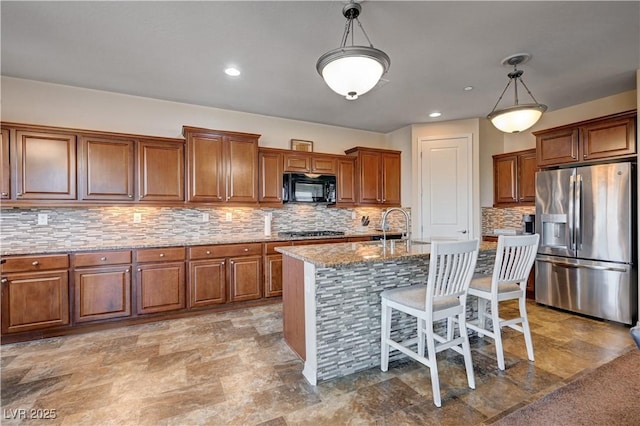 kitchen featuring light stone countertops, an island with sink, decorative light fixtures, and appliances with stainless steel finishes