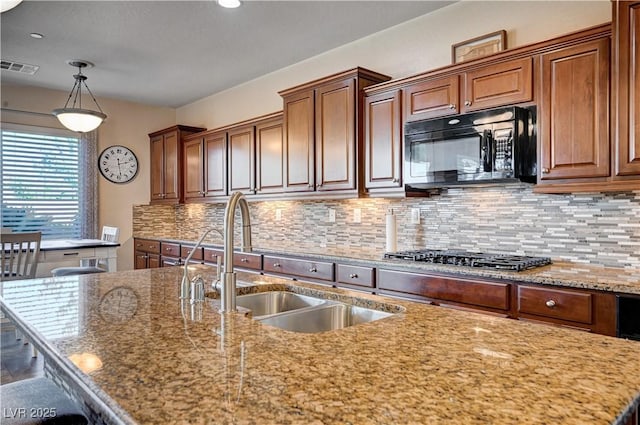 kitchen featuring light stone countertops, sink, decorative light fixtures, and stainless steel gas stovetop