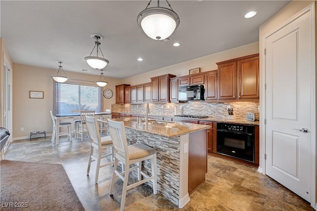 kitchen featuring sink, tasteful backsplash, decorative light fixtures, a center island with sink, and black appliances