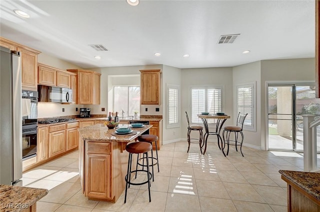 kitchen with a breakfast bar, a center island, light tile patterned floors, appliances with stainless steel finishes, and light stone counters