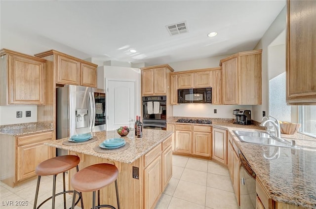 kitchen featuring black appliances, a center island, light stone countertops, and light tile patterned floors