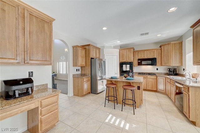 kitchen featuring a breakfast bar, black appliances, sink, a kitchen island, and light tile patterned flooring