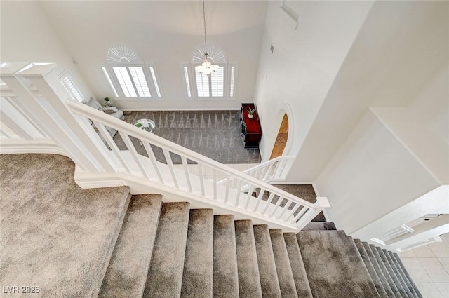 stairway with tile patterned flooring, a towering ceiling, and a chandelier