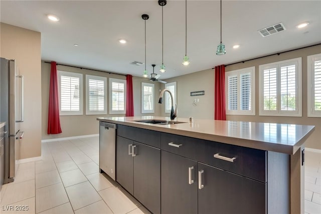 kitchen with pendant lighting, sink, light tile patterned floors, an island with sink, and appliances with stainless steel finishes