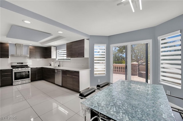 kitchen with stainless steel appliances, wall chimney range hood, decorative backsplash, dark brown cabinets, and light tile patterned floors