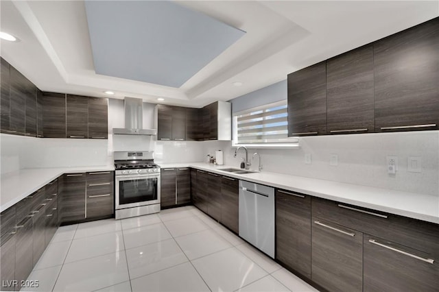 kitchen featuring wall chimney exhaust hood, stainless steel appliances, a raised ceiling, sink, and light tile patterned floors