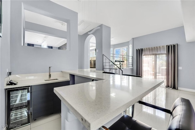 kitchen featuring kitchen peninsula, wine cooler, sink, and light tile patterned flooring