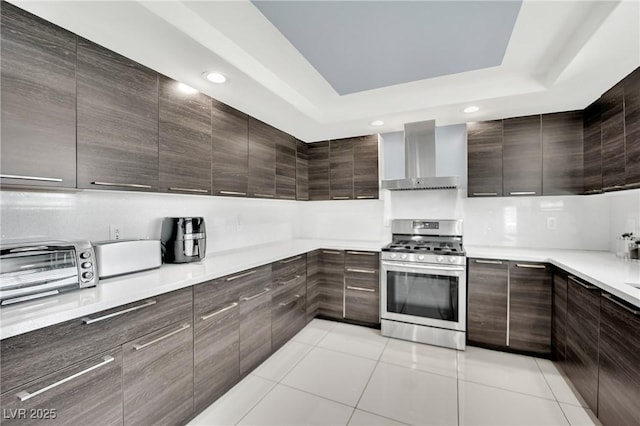 kitchen with gas range, light tile patterned floors, dark brown cabinets, and wall chimney range hood