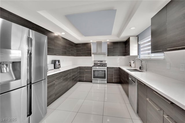 kitchen featuring stainless steel appliances, a tray ceiling, sink, wall chimney range hood, and light tile patterned floors